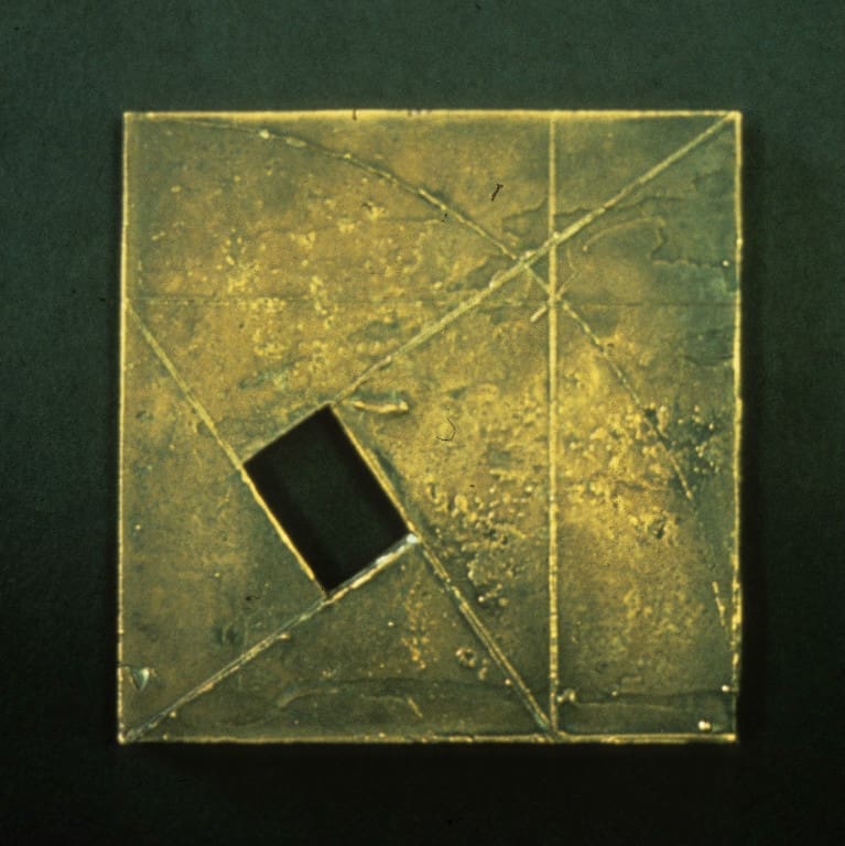 A square gold metal object with a black hole in it.