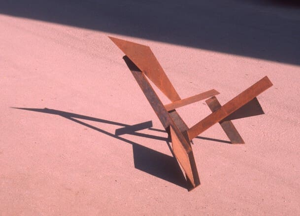 A wooden chair sitting on the ground in front of a wall.