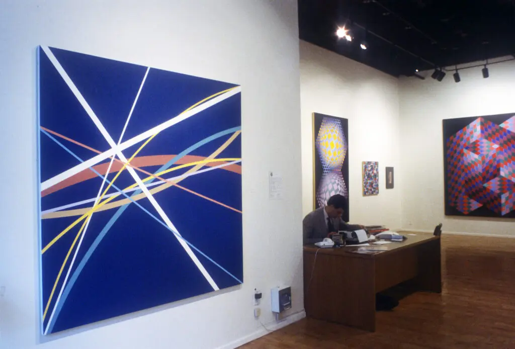 A man sitting at a desk in front of two paintings.