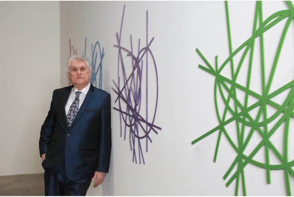 A man in suit and tie standing next to wall with art.