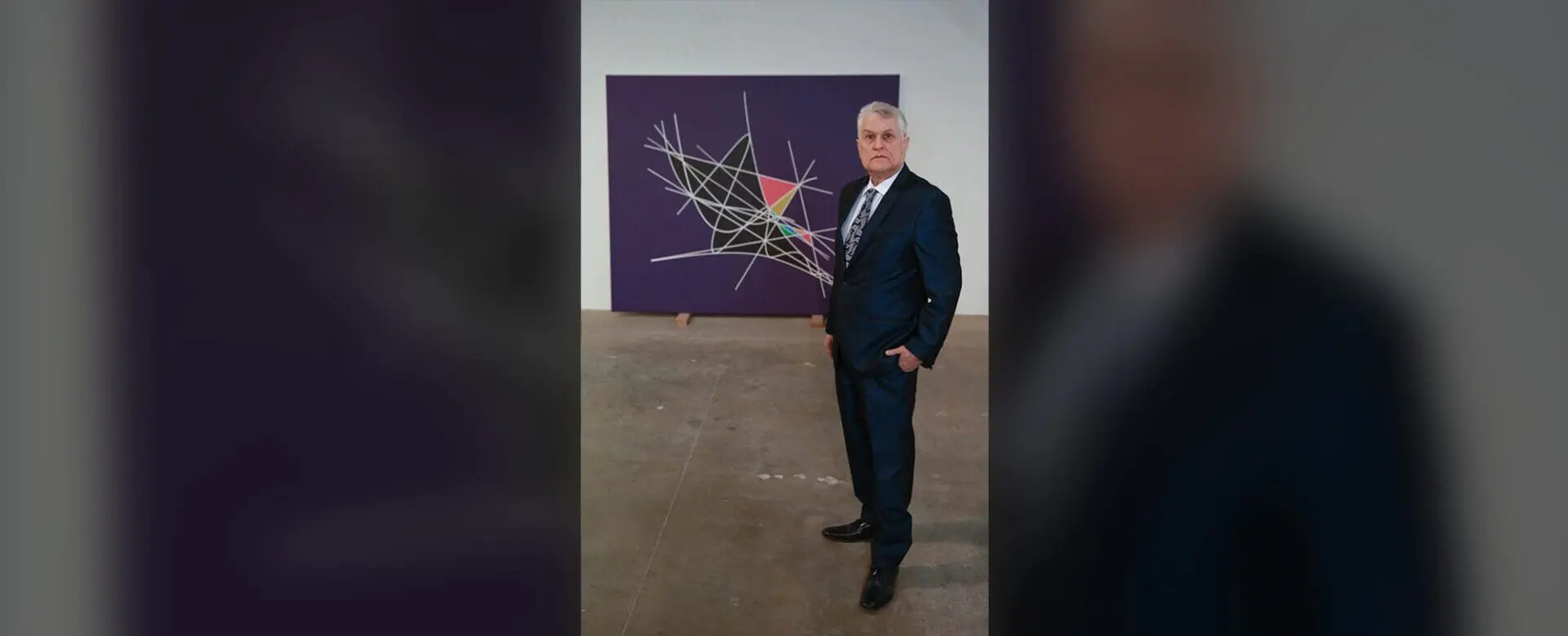 A man in a suit standing next to a painting.