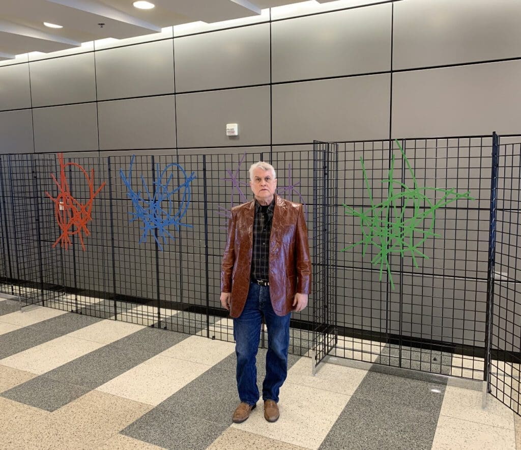 A man standing in front of a wall with colorful hand prints painted on it.