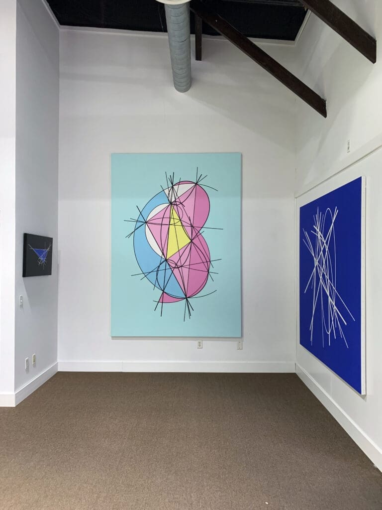 Abstract geometric paintings displayed in a modern gallery space.