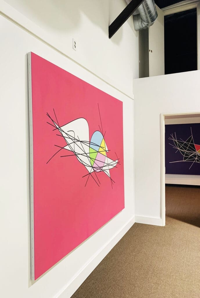 Abstract art with geometric shapes on a bold pink background in a modern gallery.