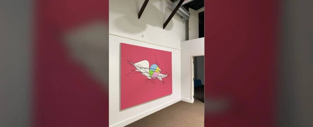 Abstract art painting with vibrant colors on a pink canvas in a modern gallery.
