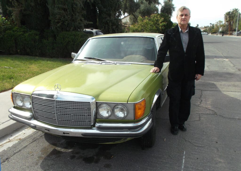 Person standing next to a vintage green Mercedes-Benz car.