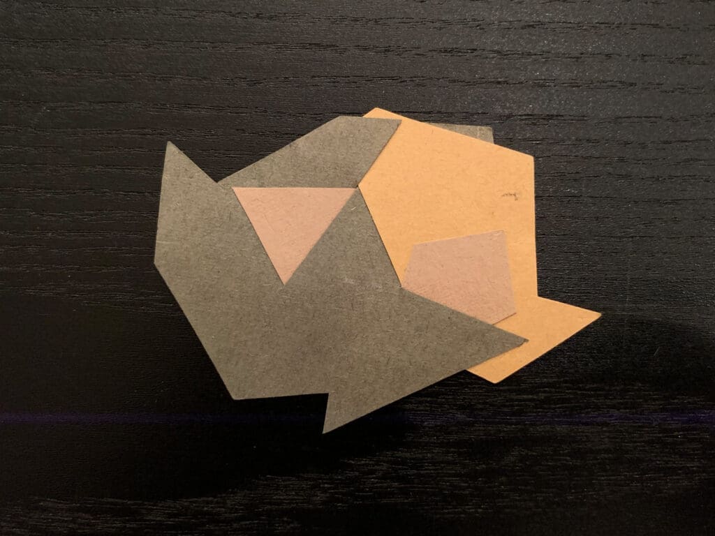 An abstract paper cutout with geometric shapes on a dark surface.
