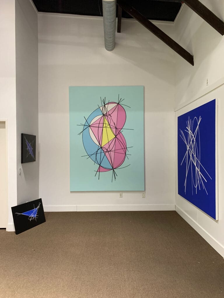 Abstract geometric paintings displayed in a minimalist gallery corner.
