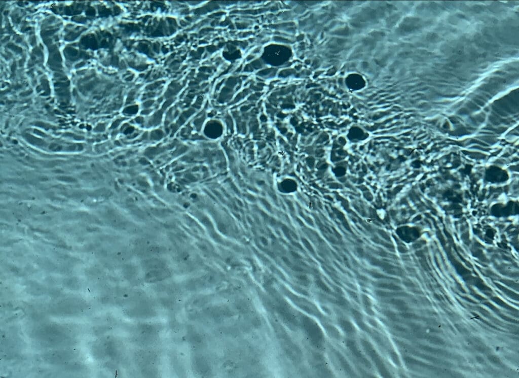 Rippling water surface with dark spots and light reflections.