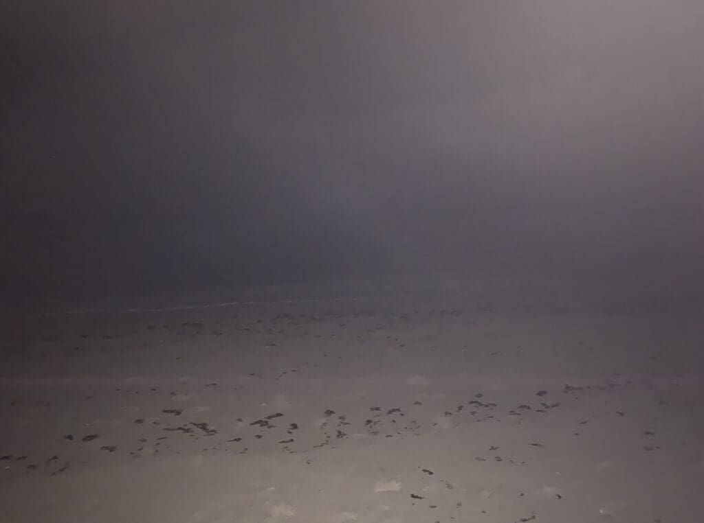 A foggy, empty beach with faint footprints in the sand.