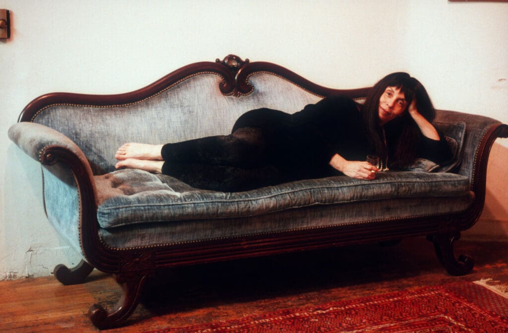 Woman in black dress reclining on vintage sofa with ornate wooden frame.