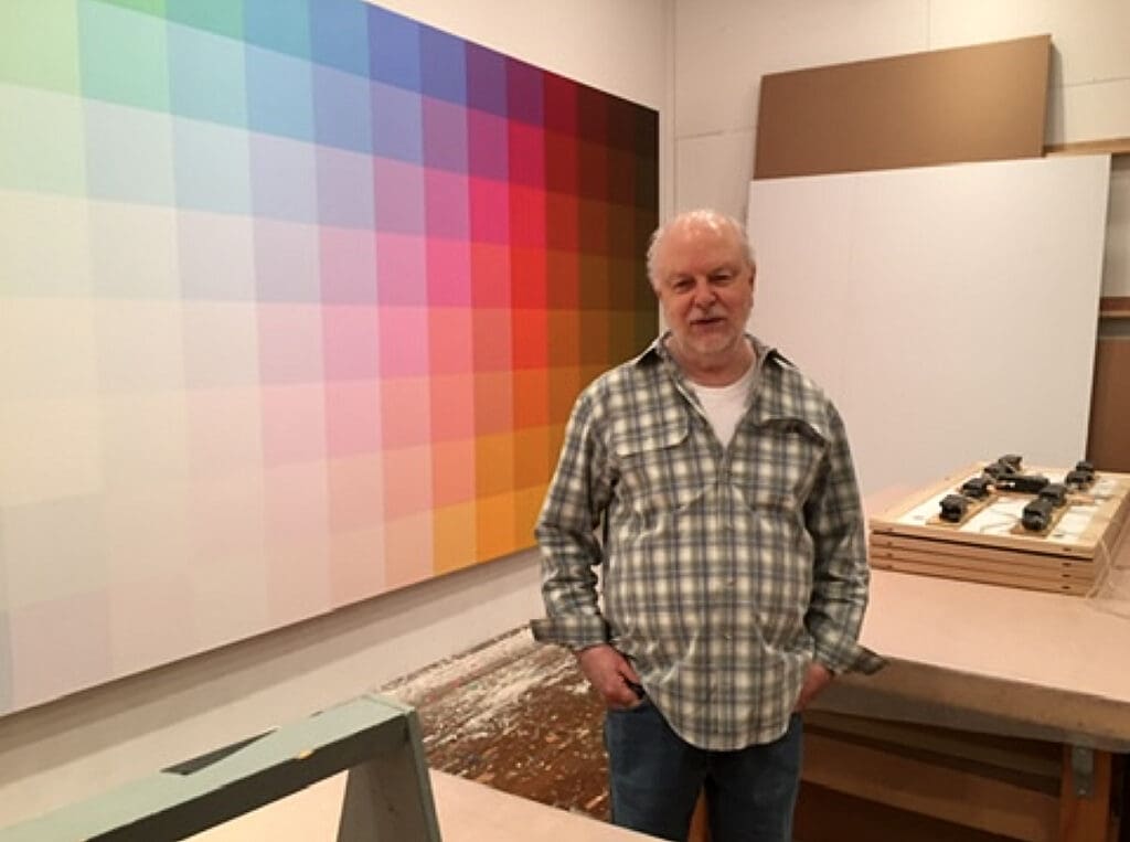 Man standing in front of a large colorful pixel art piece indoors.