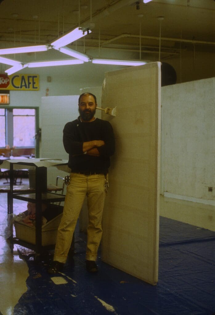 Man standing casually in a dimly lit room with industrial decor.