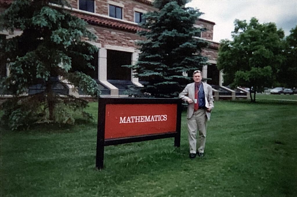 Man standing beside mathematics building sign.