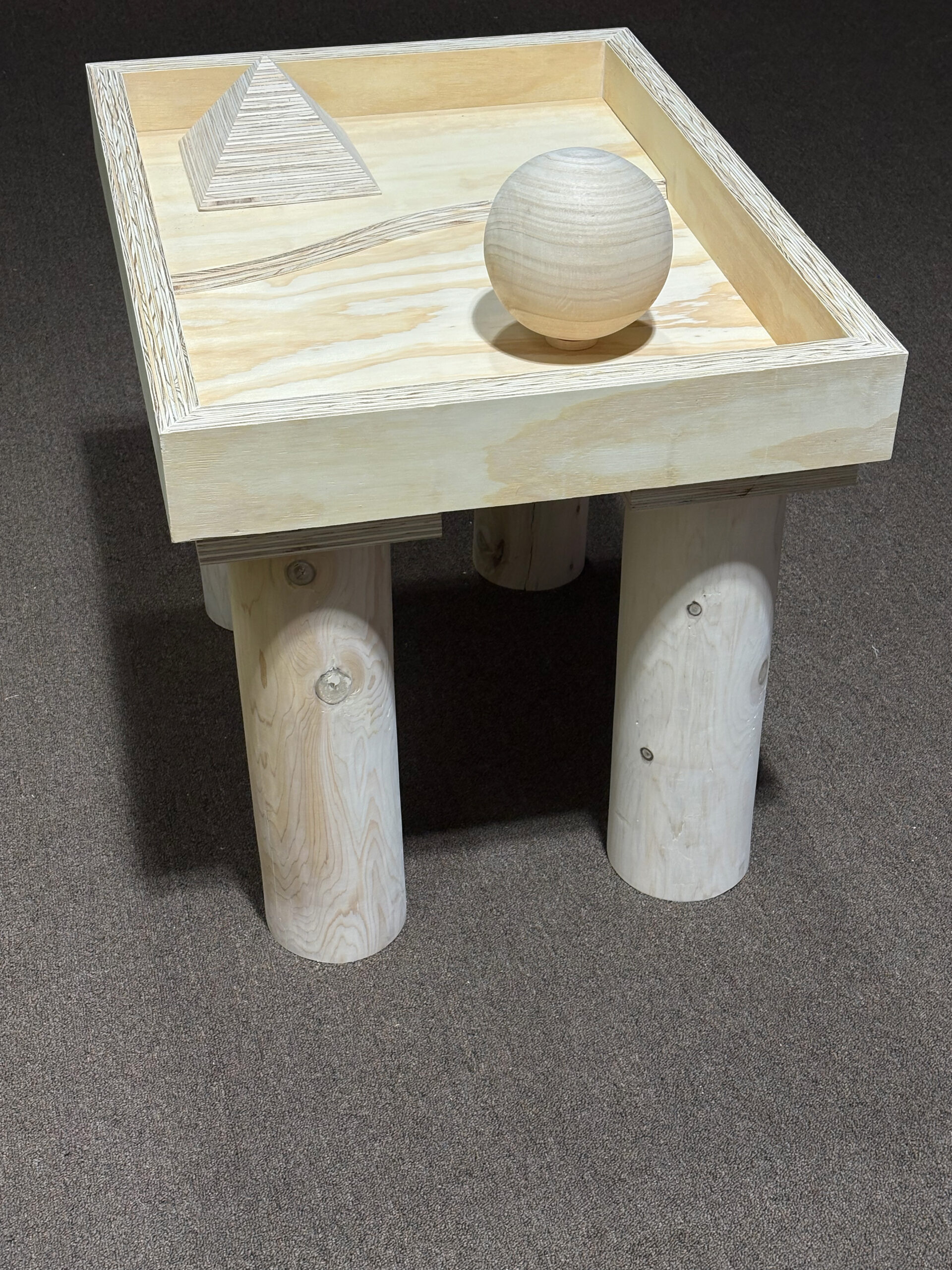 A wooden table with four cylindrical legs and a wooden sphere on top.