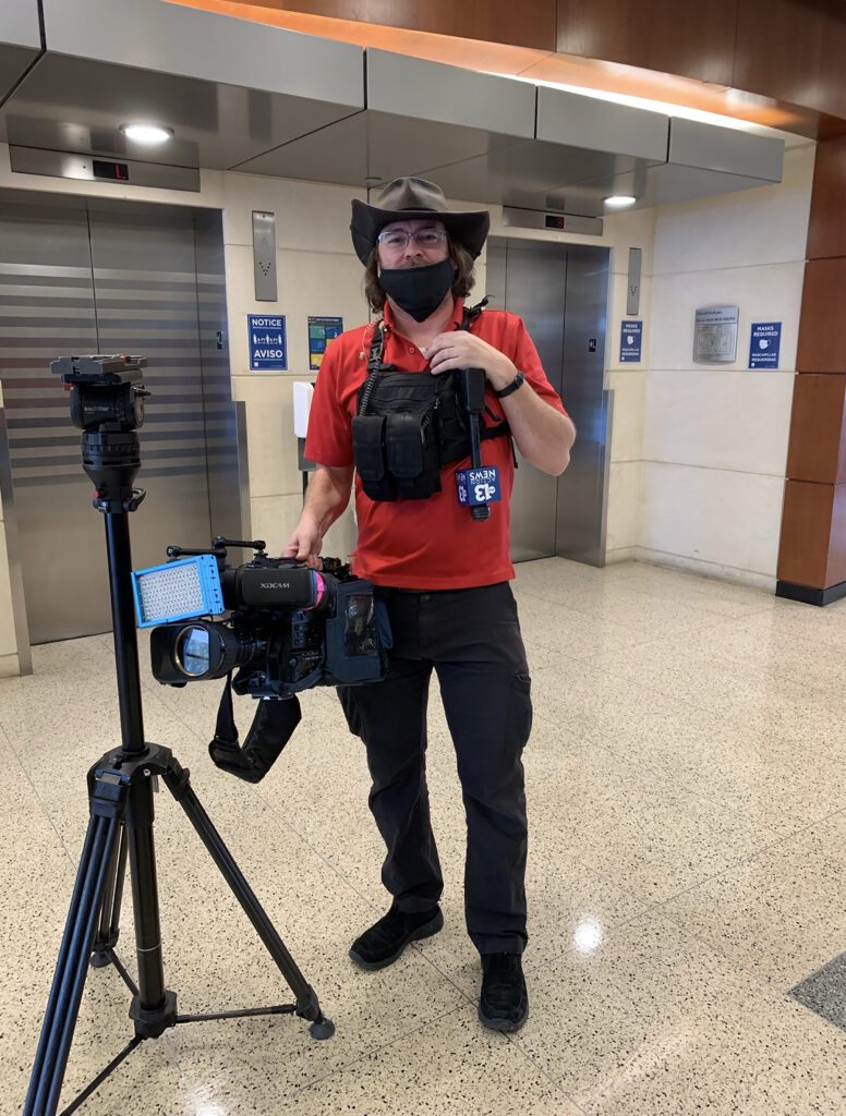 News camera operator wearing hat and mask