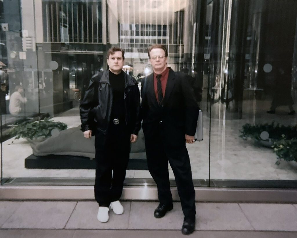 Two men posing outside glass office building