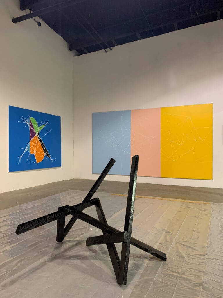 Leaning black wood sculpture with canvases