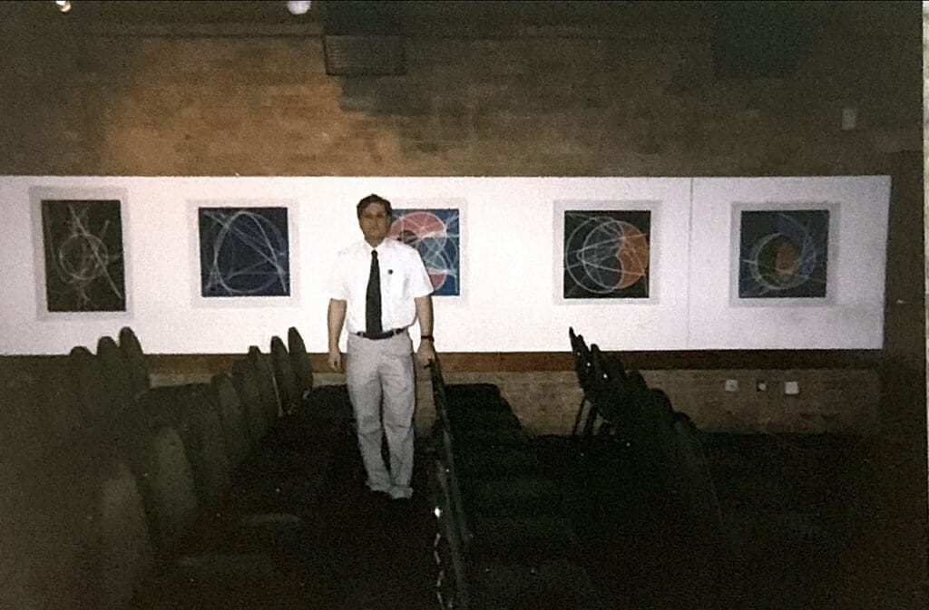 White-shirted man amid framed abstract artworks