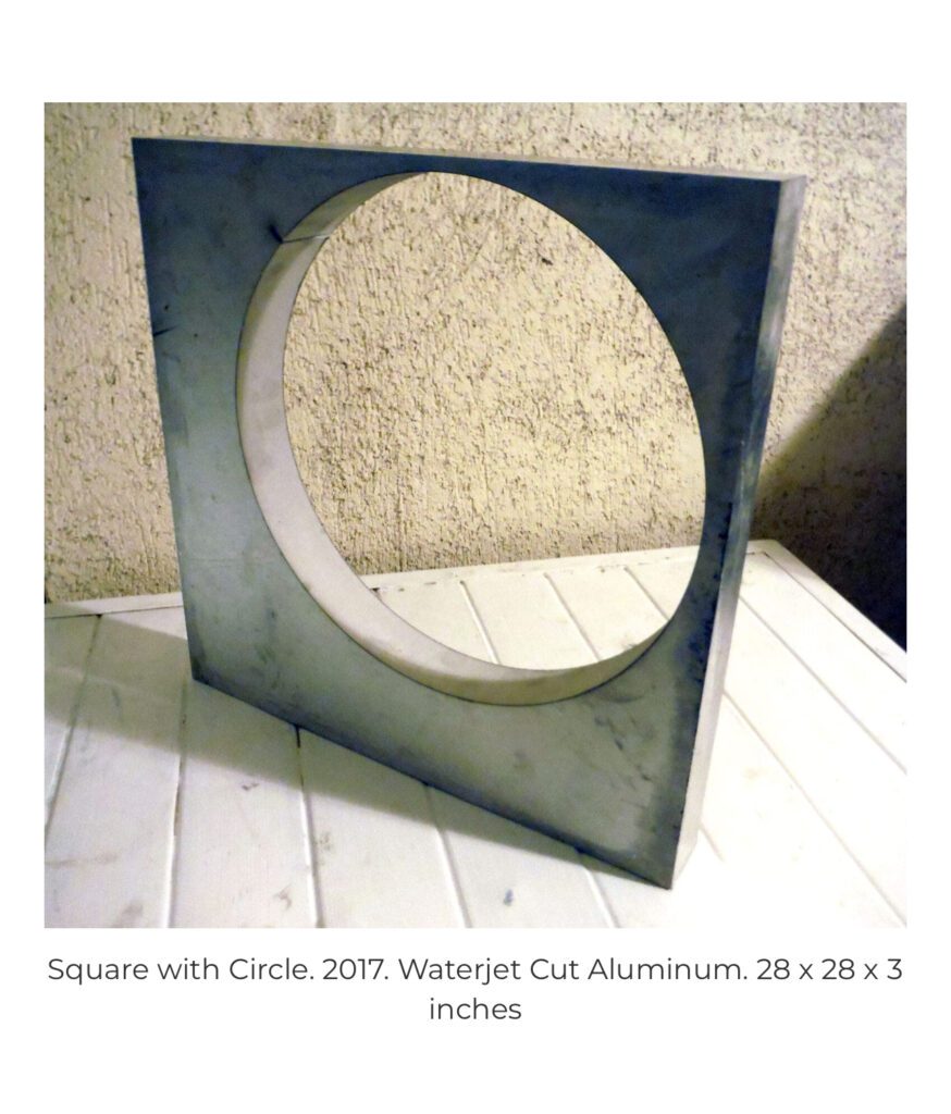 Metal square sculpture with circular cutout on table
