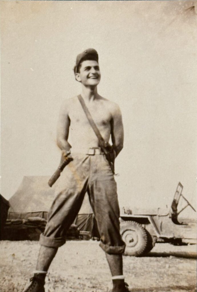 Smiling shirtless soldier posing near military jeep