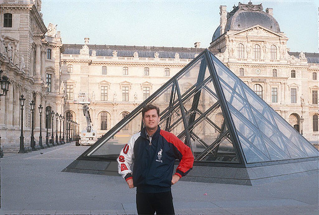 Man posing in front of Louvre glass pyramid