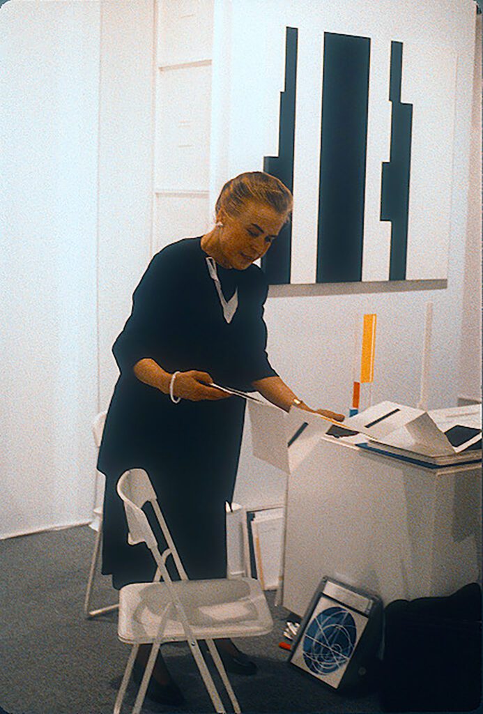 Gallery attendant arranging prints beside modern paintings